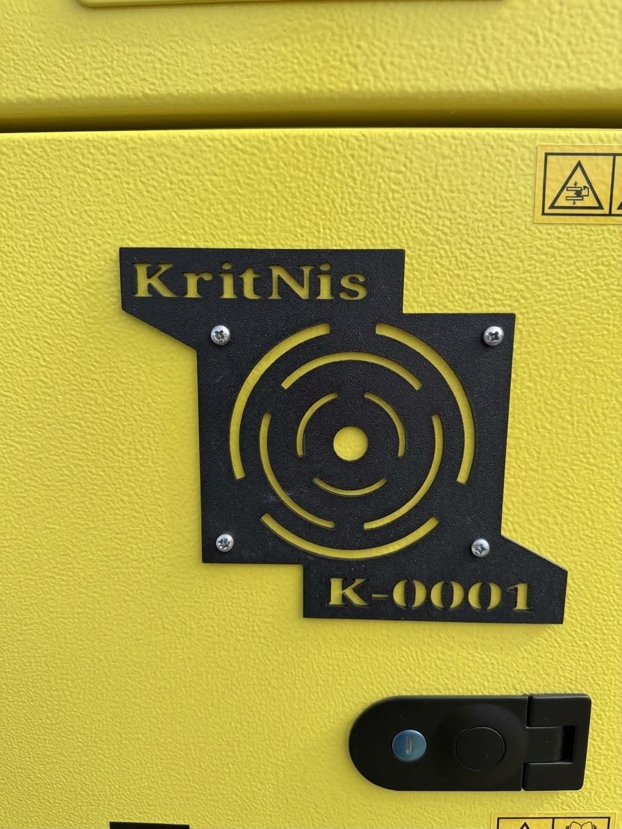 Typenschild am KritNis-Turm: Zeichen von KritNis mit drei Ringen und der Kennung K-0001, ausgestanzt in eine schwarze Platte.